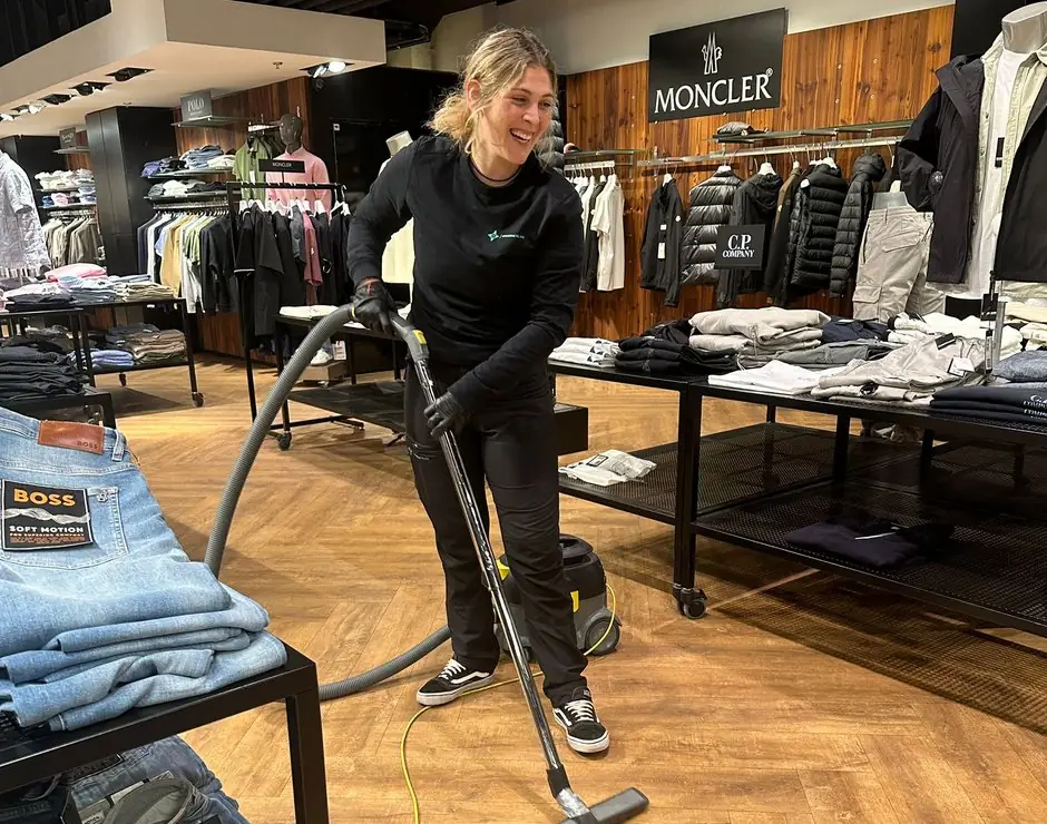Medarbejder fra Rengøring Til Dig støvsuger gulvet i en tøjbutik