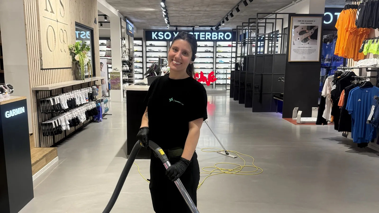 Smilende medarbejder fra Rengøring Til Dig støvsuger i en butik